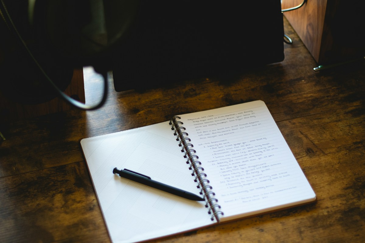 An open notebook and pen on a wooden desk